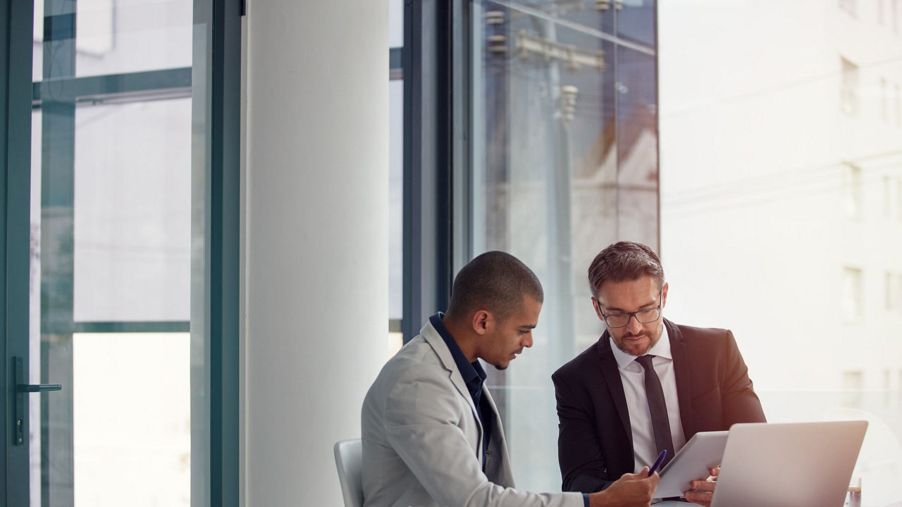 Two business people sitting at a table and looking at a laptop.