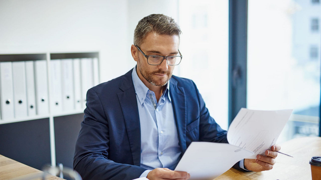 A businessman is sitting at a desk and looking at papers.
