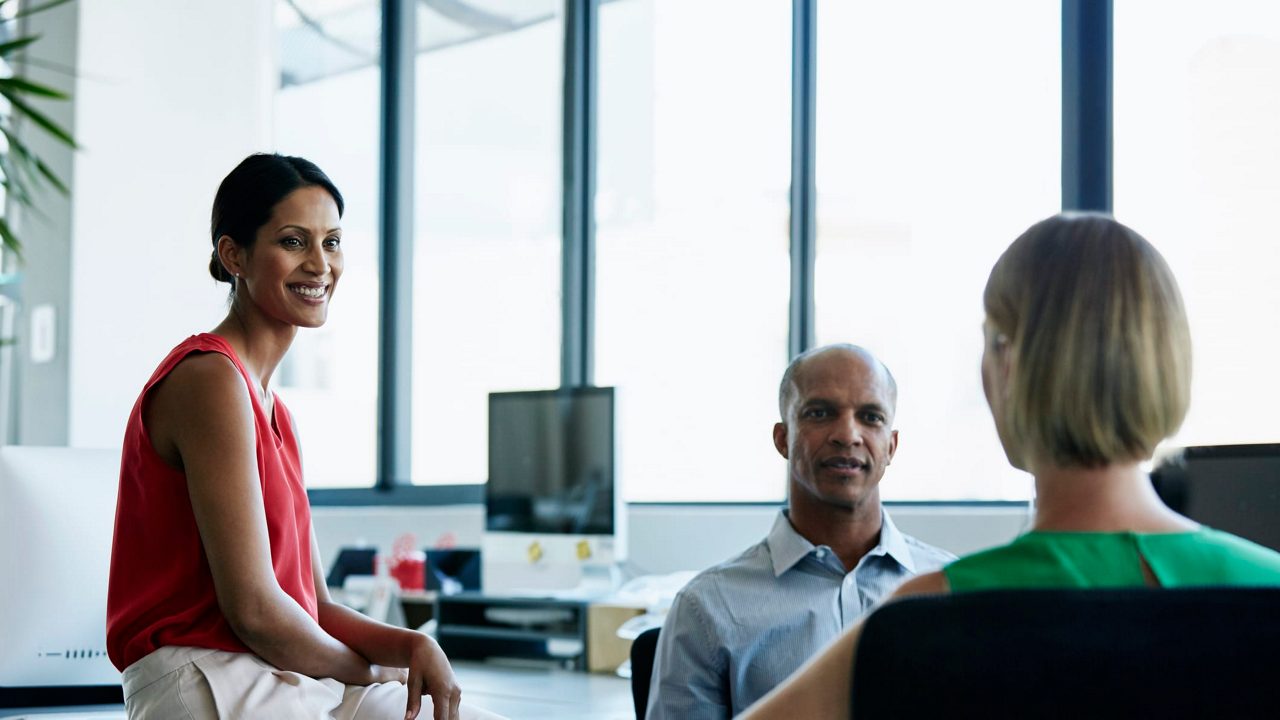 Three people sitting in an office talking to each other.