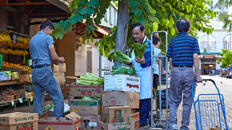 A group of men standing next to a cart full of fruit and vegetables.