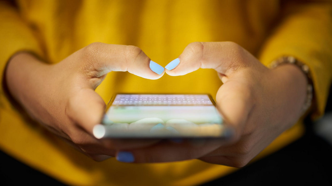 A woman's hands making a heart shape on a smartphone.