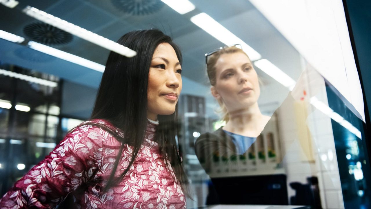 Two women standing in front of a glass window.