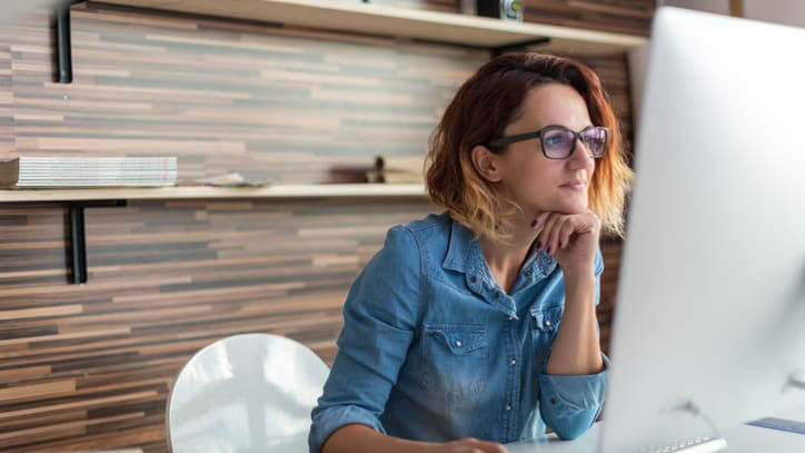 A woman wearing glasses is sitting at a desk in front of a computer.