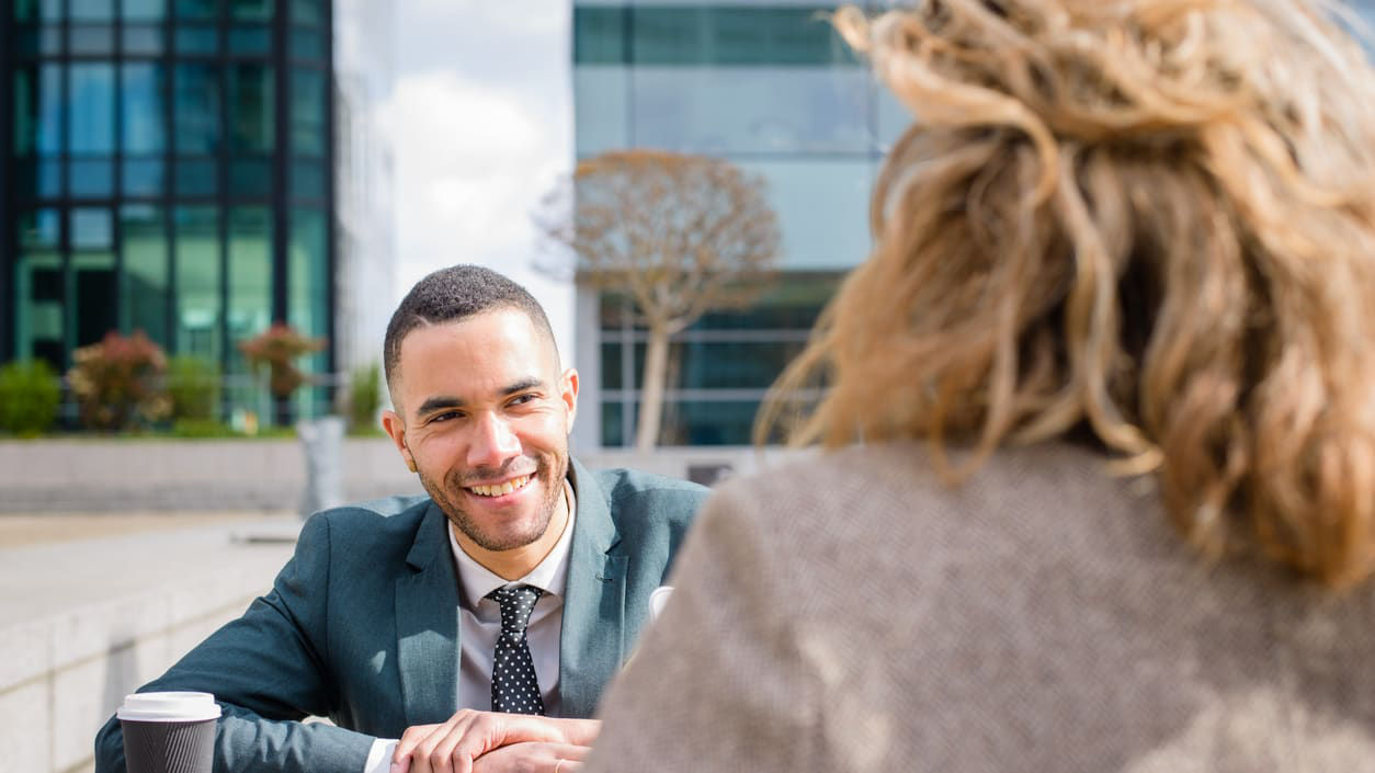 A man and woman are having a conversation at an outdoor table.