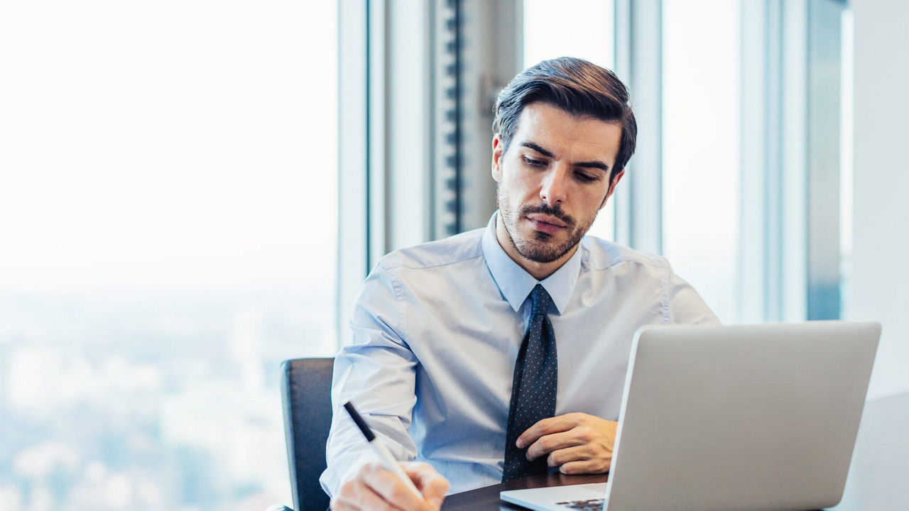 A businessman sitting at a desk with a laptop and a pen.