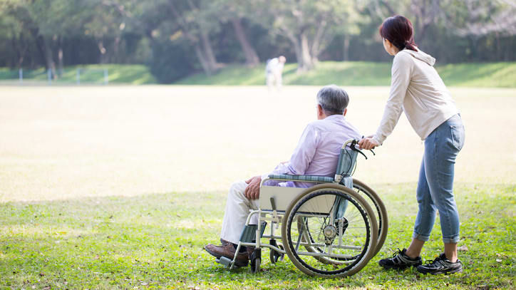A woman is helping an elderly man in a wheelchair in a park.