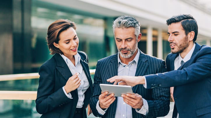 Three business people looking at a tablet.