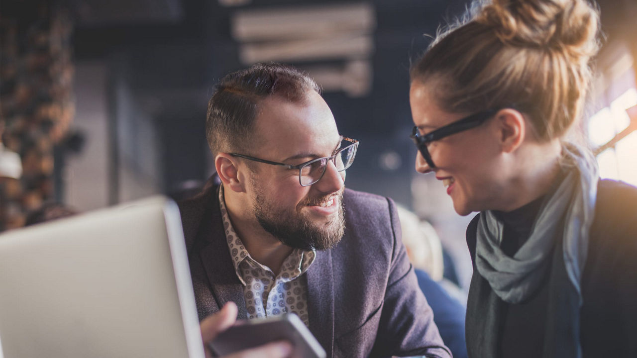 A man and a woman looking at a laptop in a coffee shop.