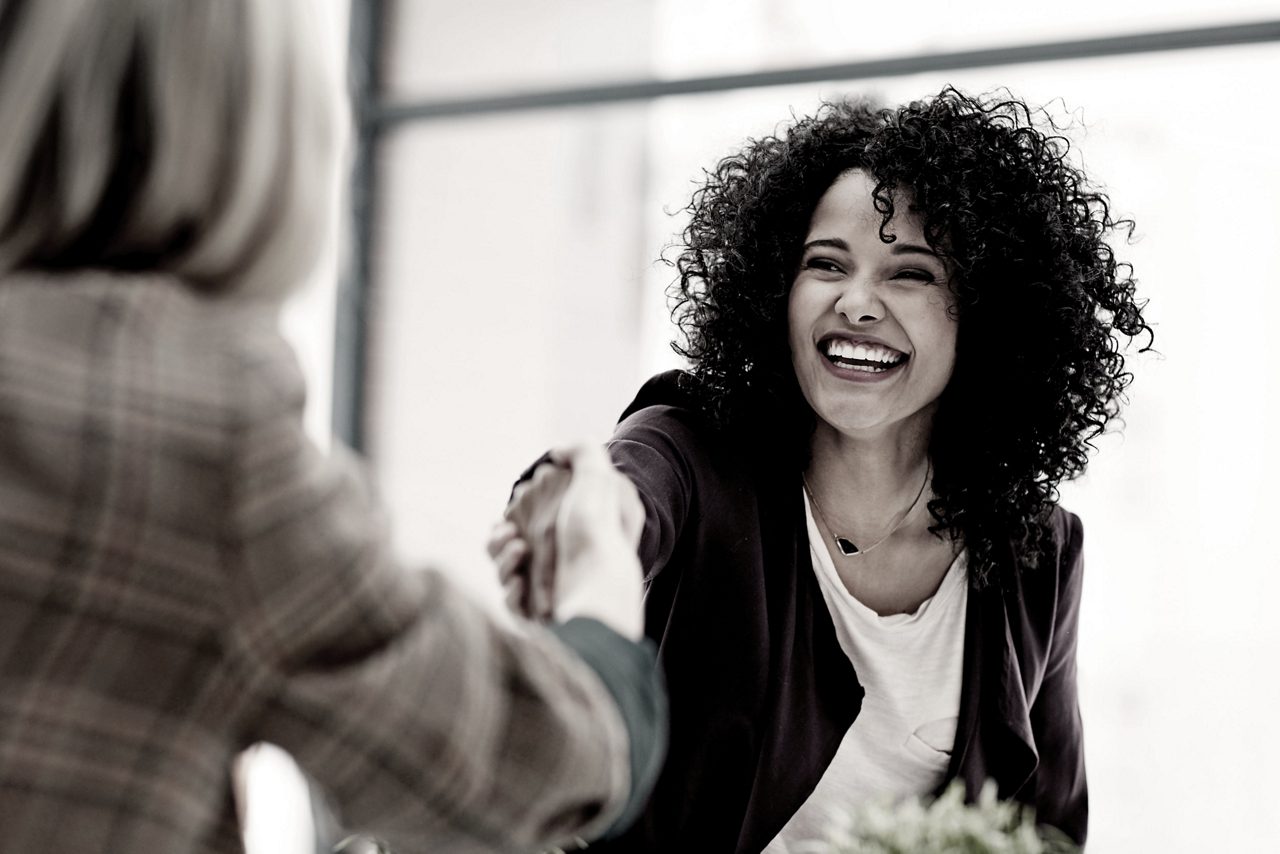 A professional woman smiles and shakes the hand of another woman.