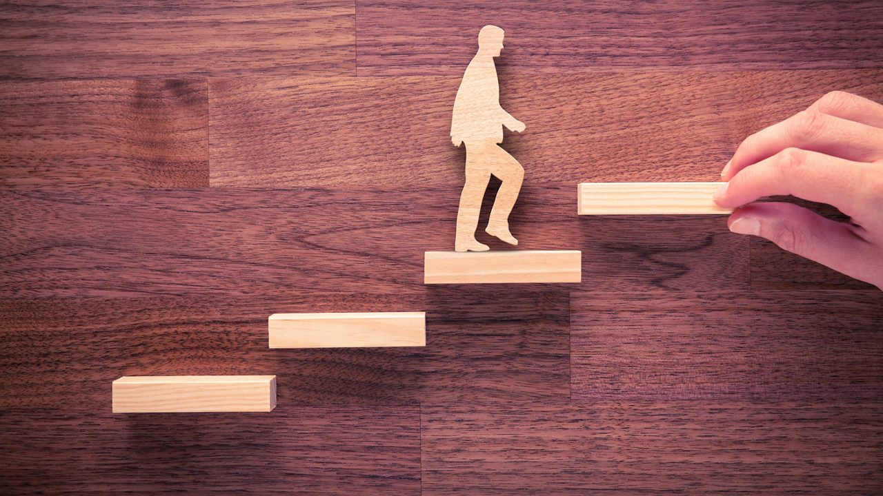 A hand reaching up a set of wooden stairs.