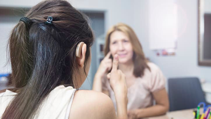 A woman is talking to another woman at a desk.