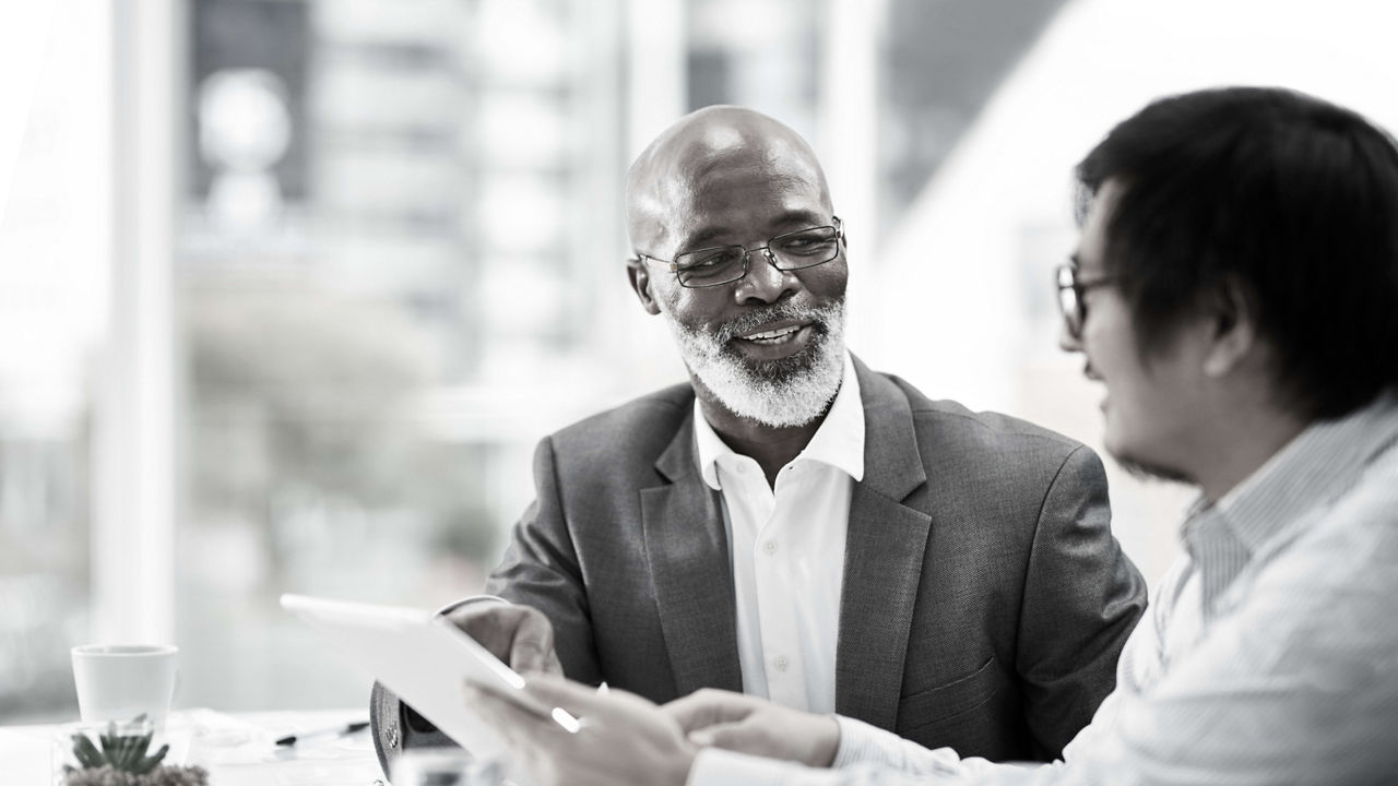 Black and white photo of two business men talking at a meeting.