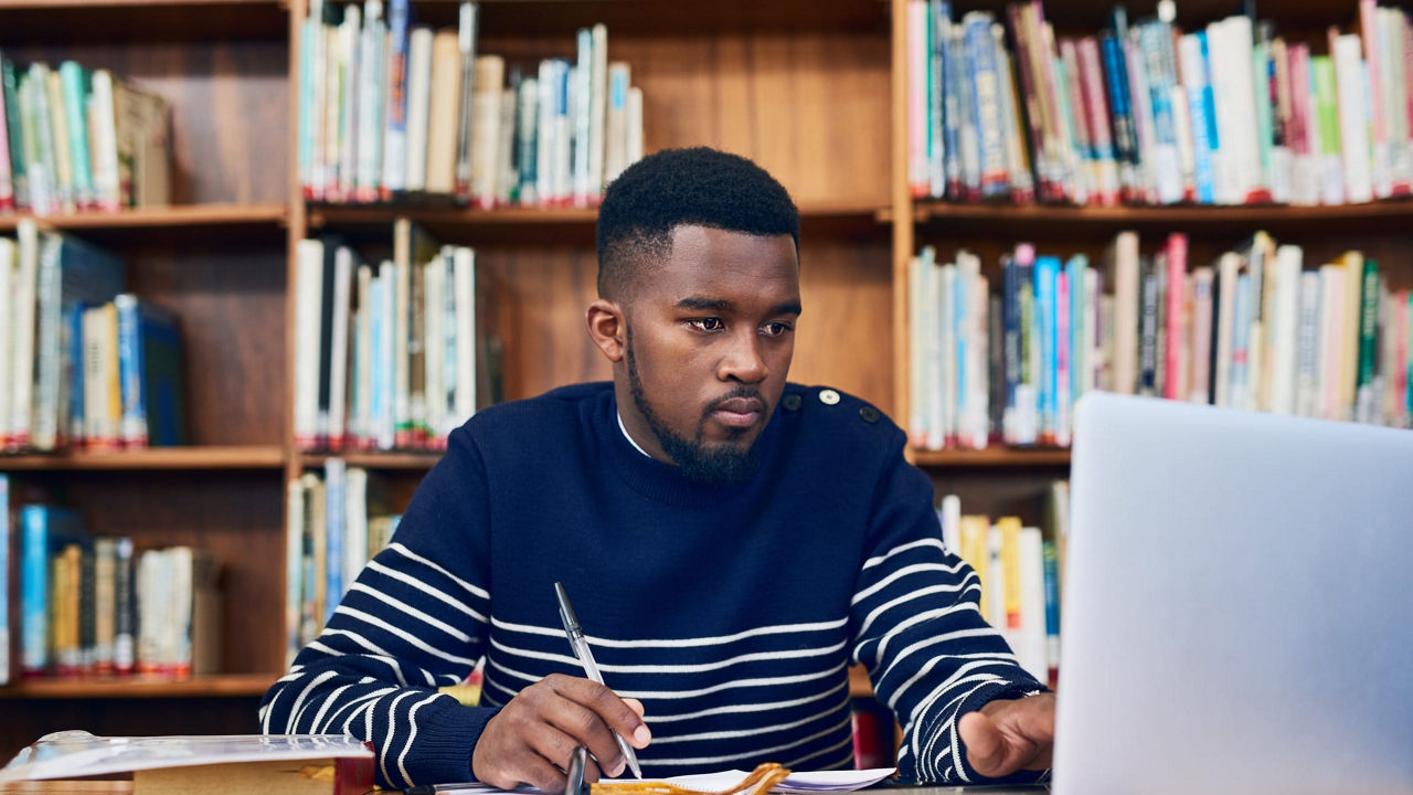 A man sitting at a desk with a laptop in front of bookshelves.