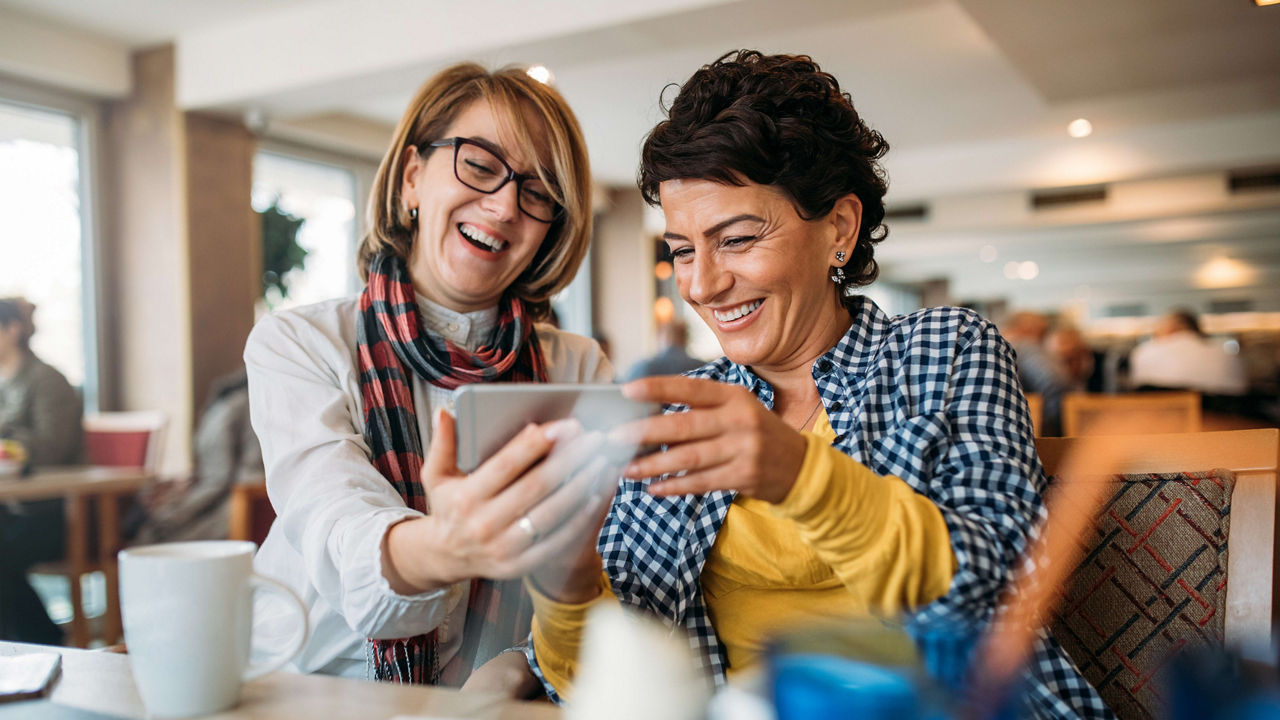 Two women looking at a tablet while sitting at a restaurant.