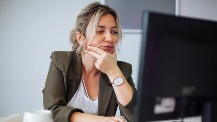 A woman sitting in front of a computer with her hand on her chin.