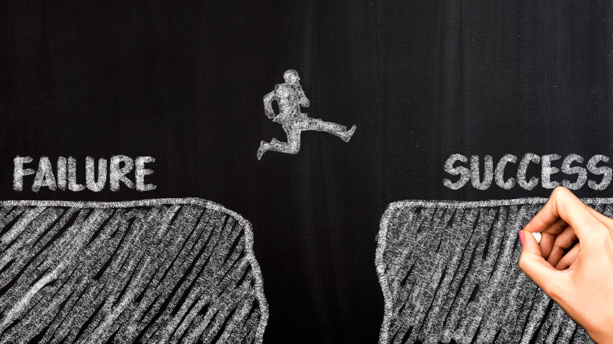 A hand drawing the words failure and success on a blackboard.