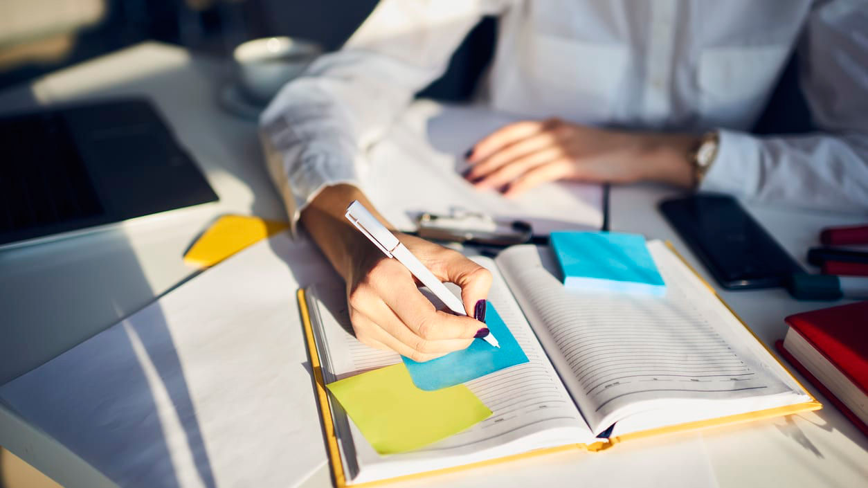 A woman is writing on a notebook at a desk.