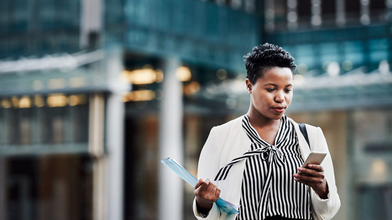 A business woman is looking at her phone while standing in front of a building.