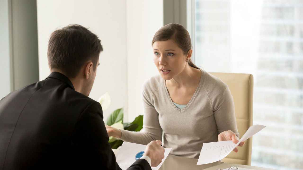 A man and woman talking at a desk in an office.