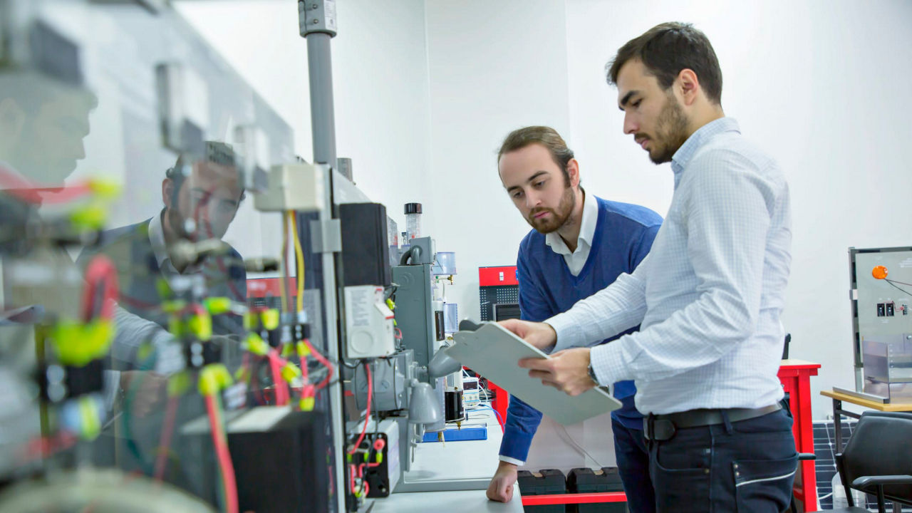 Two men standing in front of a machine in a factory.