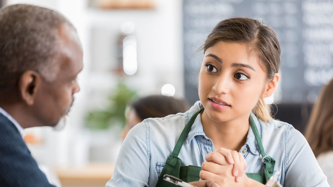 A woman talking to an older man in a coffee shop.