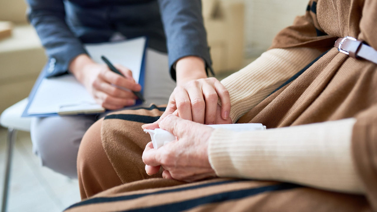 A woman is holding an elderly woman's hand in a doctor's office.