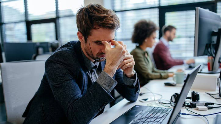 A man is holding his head in front of a computer screen.