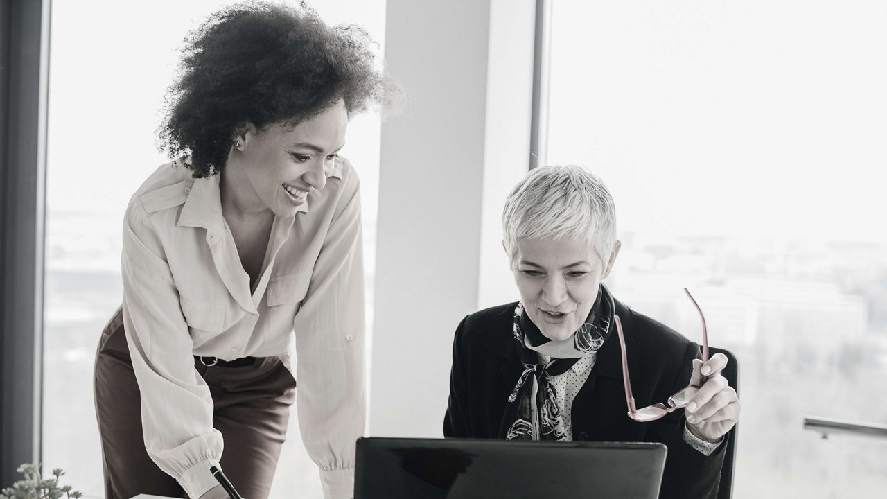 Two women working on a laptop in an office.