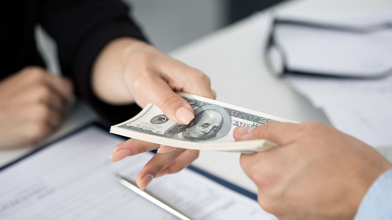 A person handing a dollar bill to another person at a desk.