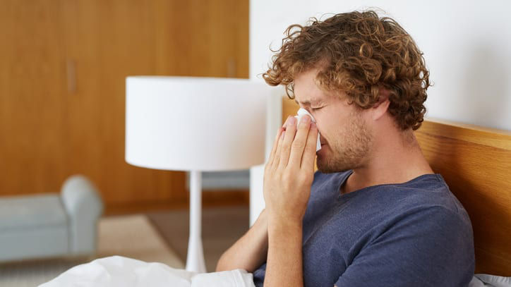 A man sneezing in bed.