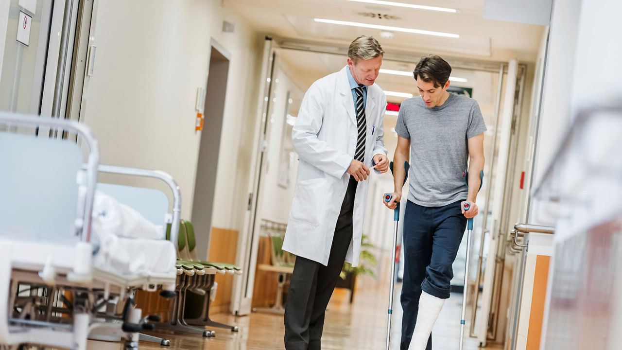 A man with a broken leg is walking down a hospital corridor.