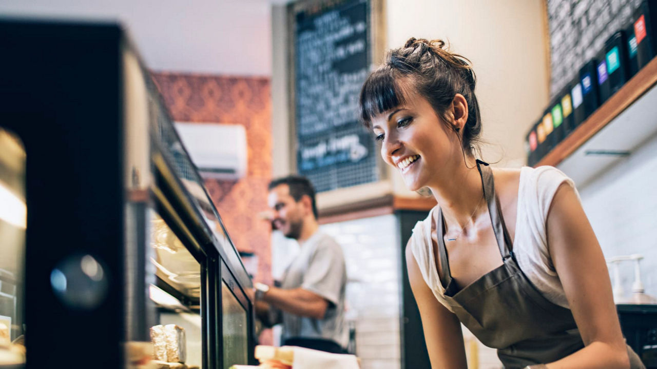A woman in an apron is putting food into a display case.