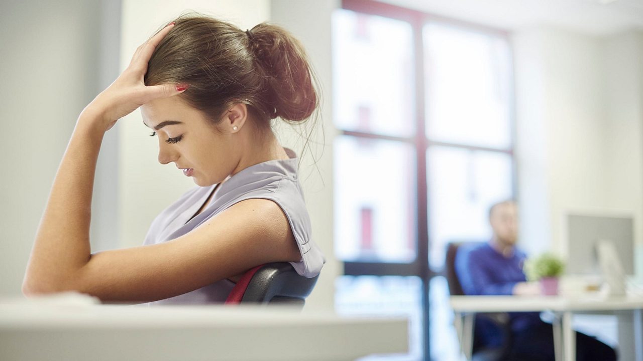 A woman is sitting at a desk with her hands on her head.