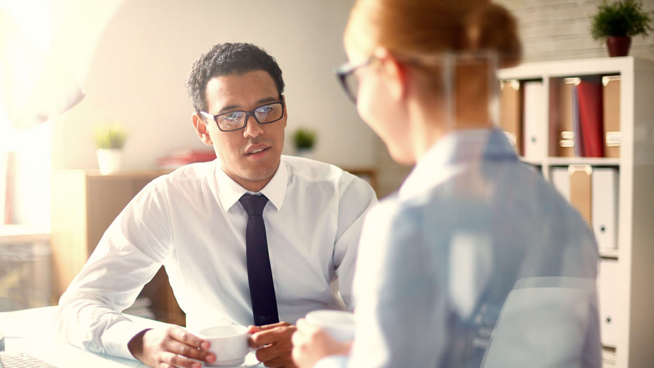 A man and woman talking at a desk in an office.