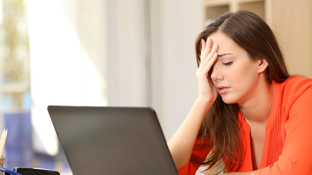 A woman is sitting at a desk with her hand on her head.