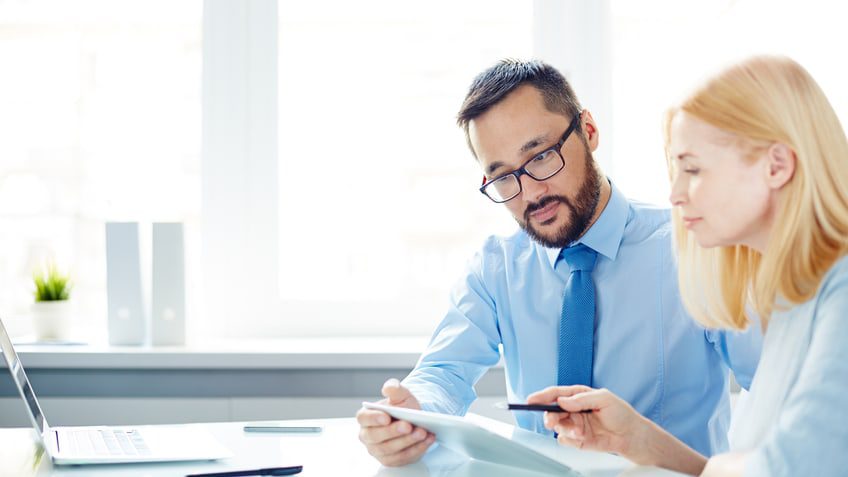 A man and woman are sitting at a desk looking at a laptop.