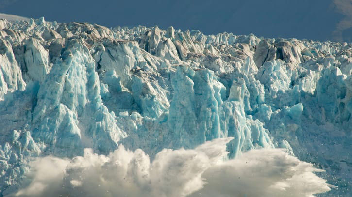 A glacier is exploding in front of a large body of water.