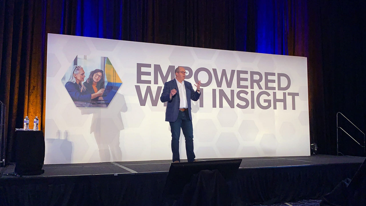 A man standing on stage at an event with the word empowered insight.