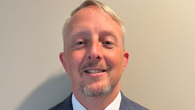 A man in a suit and tie smiling in front of a wall.