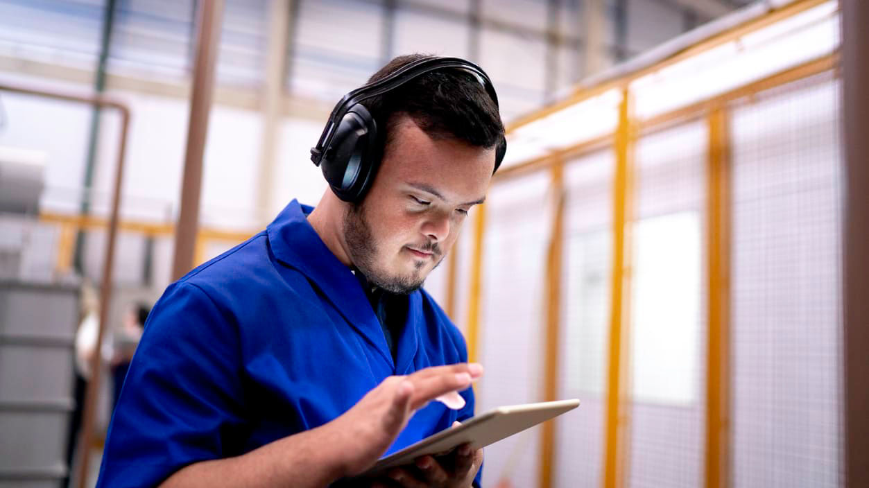 A man wearing headphones is using a tablet in a factory.