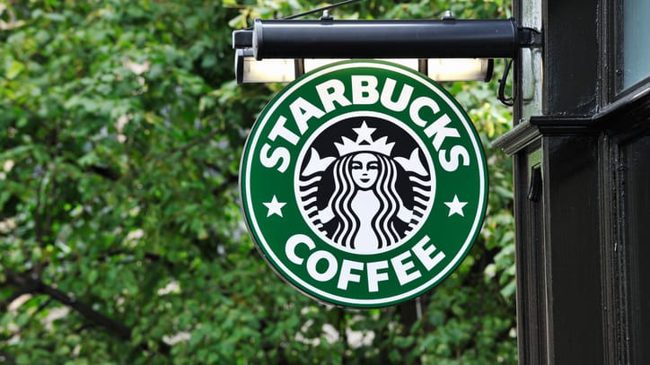 A starbucks coffee sign hangs from the side of a building.