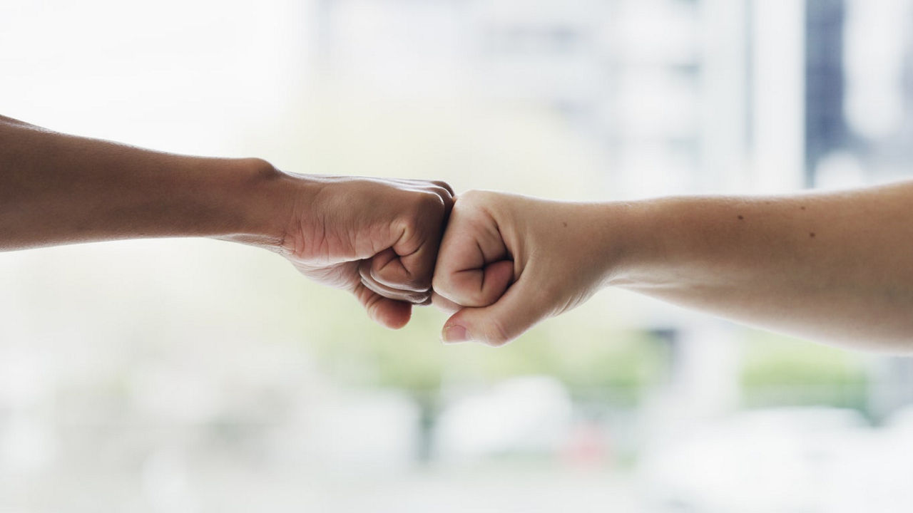 Two people fist bumping each other in front of a building.