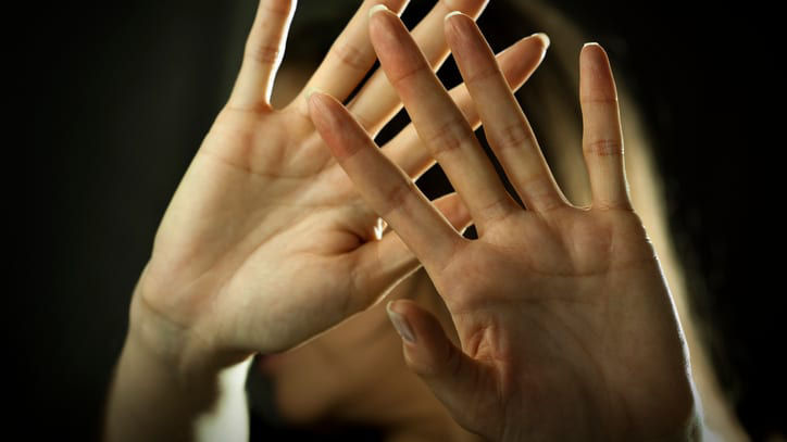A woman is holding her hands up in front of a dark background.