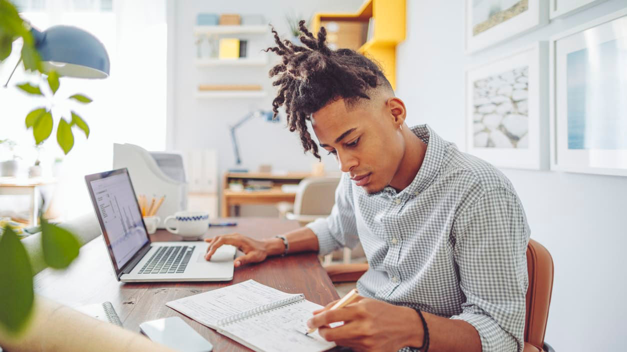 A man working at his desk with a laptop and a notebook.