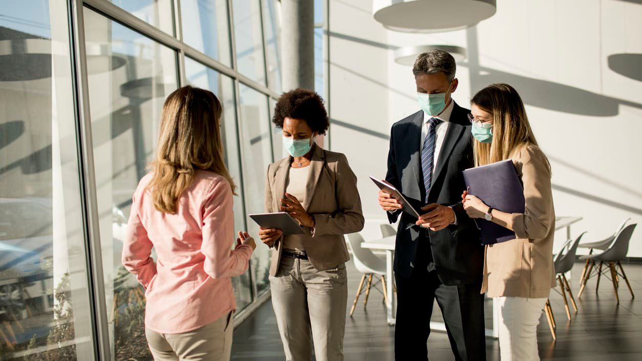 Four business people wearing face masks in an office.