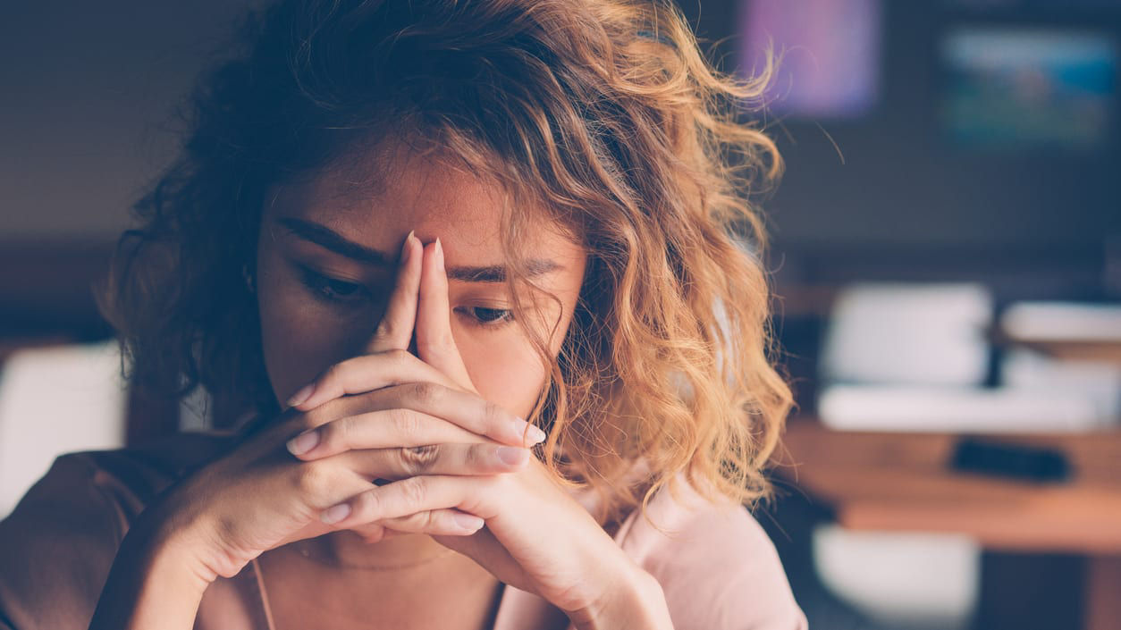 A woman clasping her hands up to her face looking concerned.