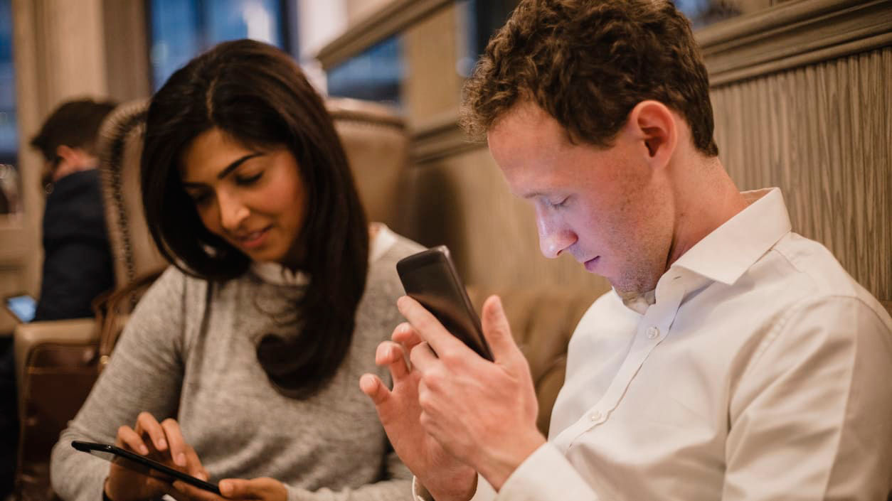 Two people sitting on a couch looking at their cell phones.