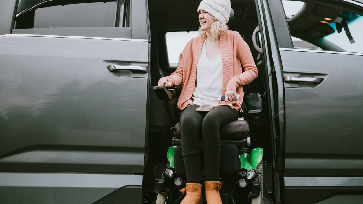 A woman in a wheelchair sitting in the door of a car.