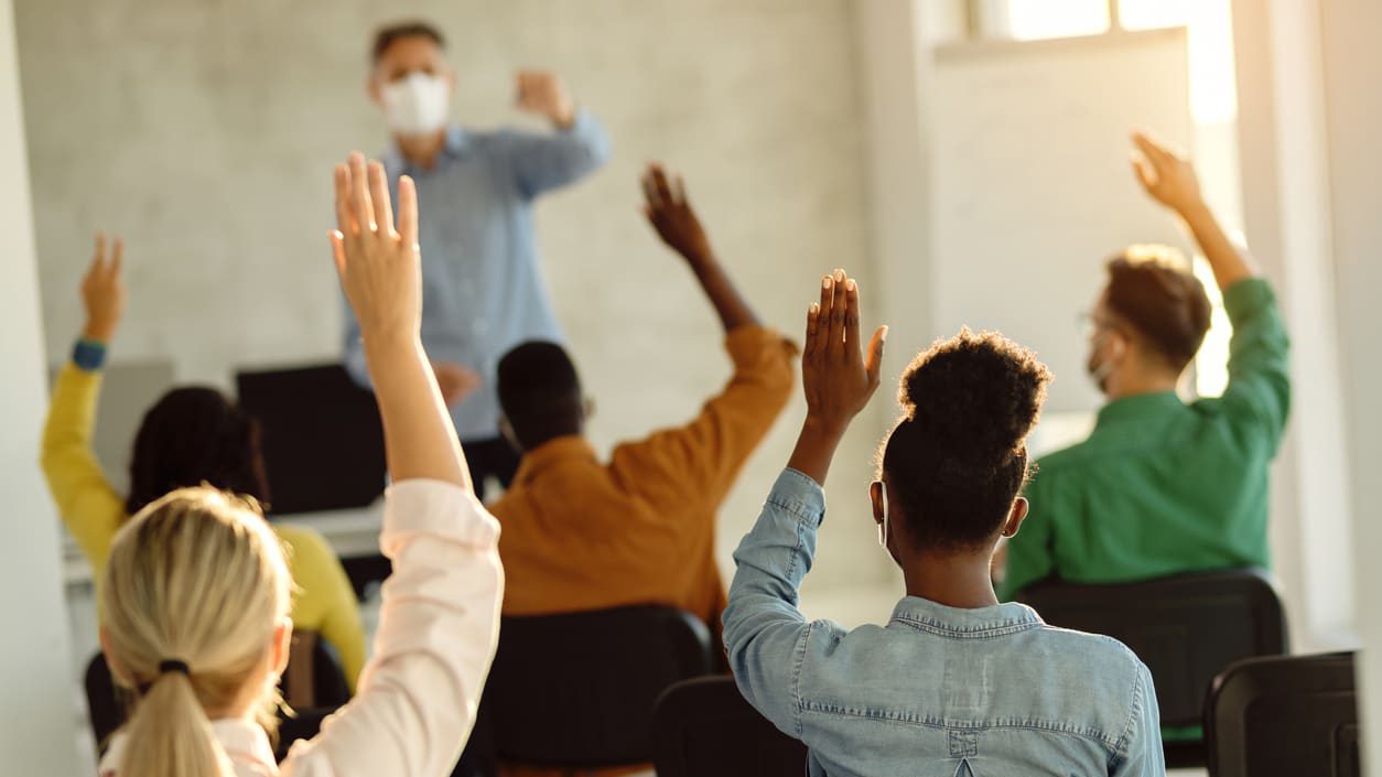 A group of people raising their hands in a classroom.