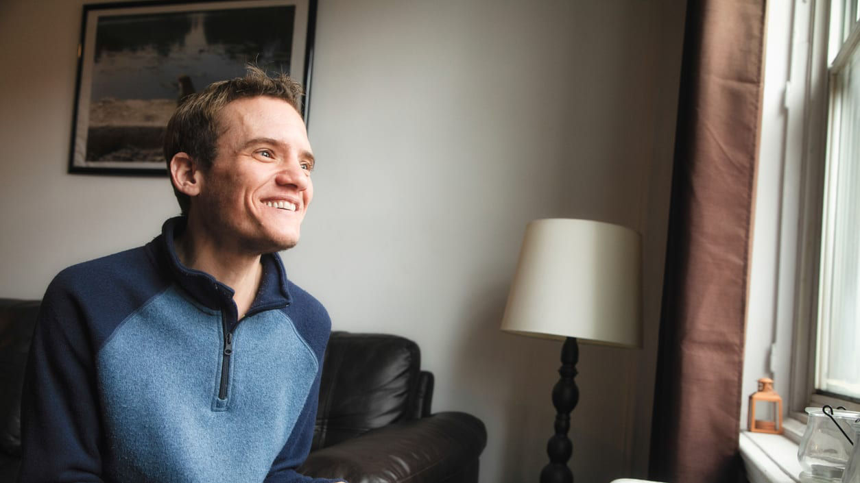 A man smiles while sitting in front of a window.